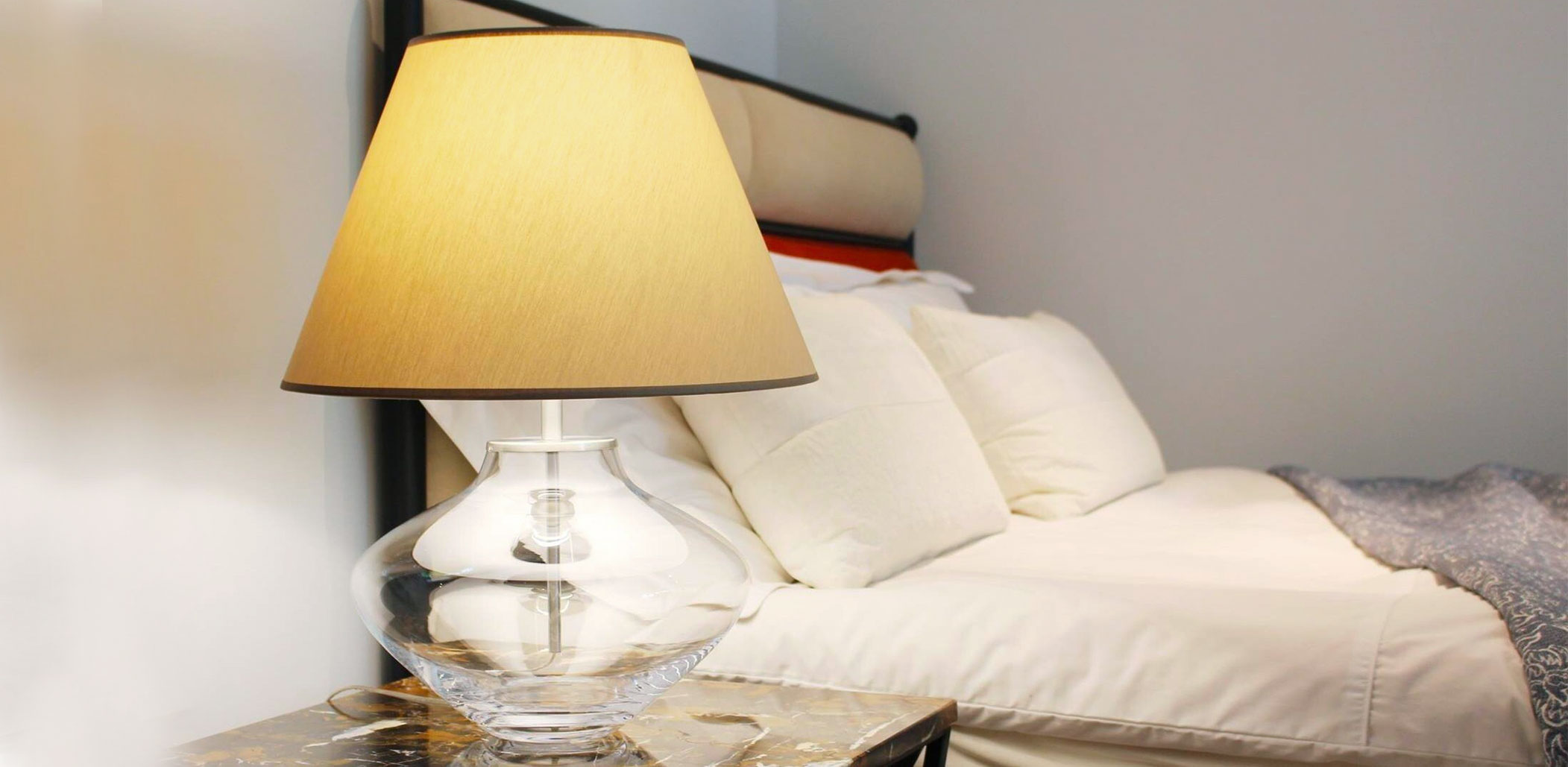 Gläserne Vasen-Tischleuchte mit Stoff-Schirm als Nachttischlampe am Bett